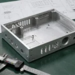 Finished CNC machined aluminum housing placed on an inspection table with caliper and technical drawing