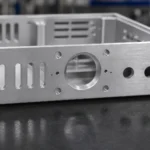 CNC machined aluminum chassis on a workbench showing internal structure, mounting holes, and machined surfaces